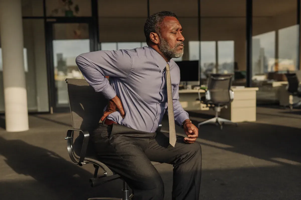 Man in an office chair holding his lower back