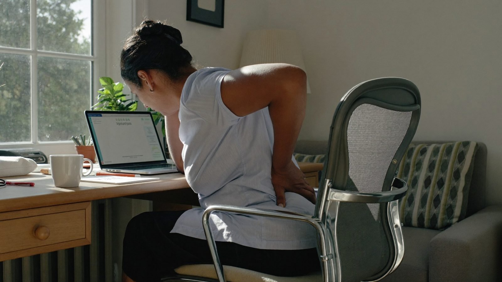 Woman at a home desk holding her lower back